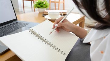 Female college student writing her homework on spiral notebook