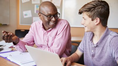 High School Tutor Giving Male Student One To One Tuition At Desk