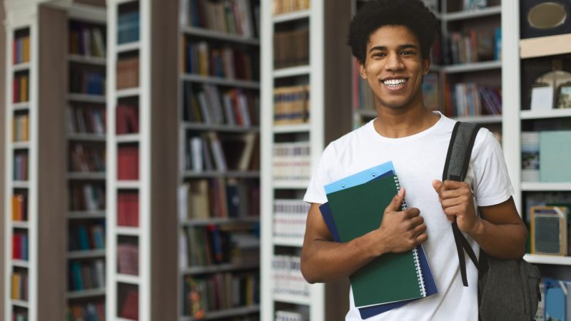 Handsome afro student posing on bookshelves background