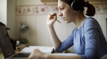 Teenage girl with headphones using laptop for studying at home