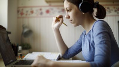 Teenage girl with headphones using laptop for studying at home